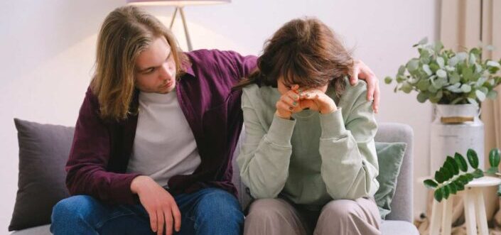 Man soothing crying sad woman on sofa