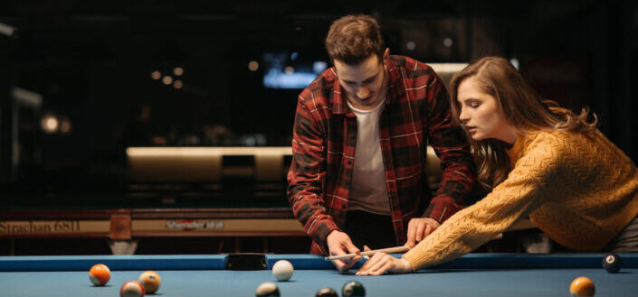 man teaching his girlfriend to play billiards