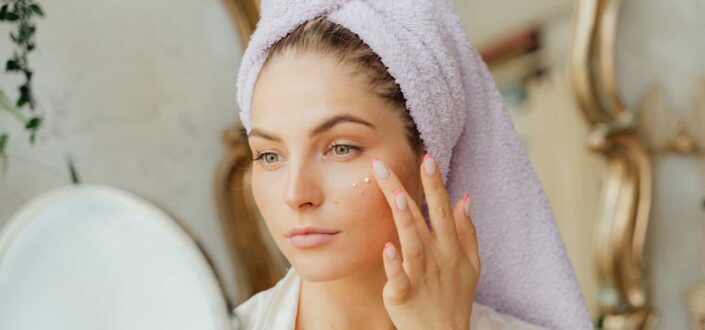 Woman with head towel applying face cream