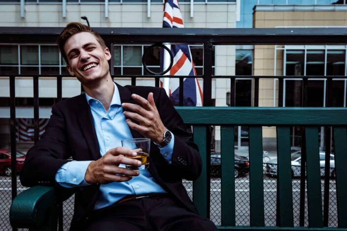man smiling while sitting and holding whisky