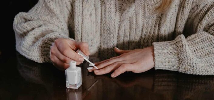 woman in gray sweater holding nail polish